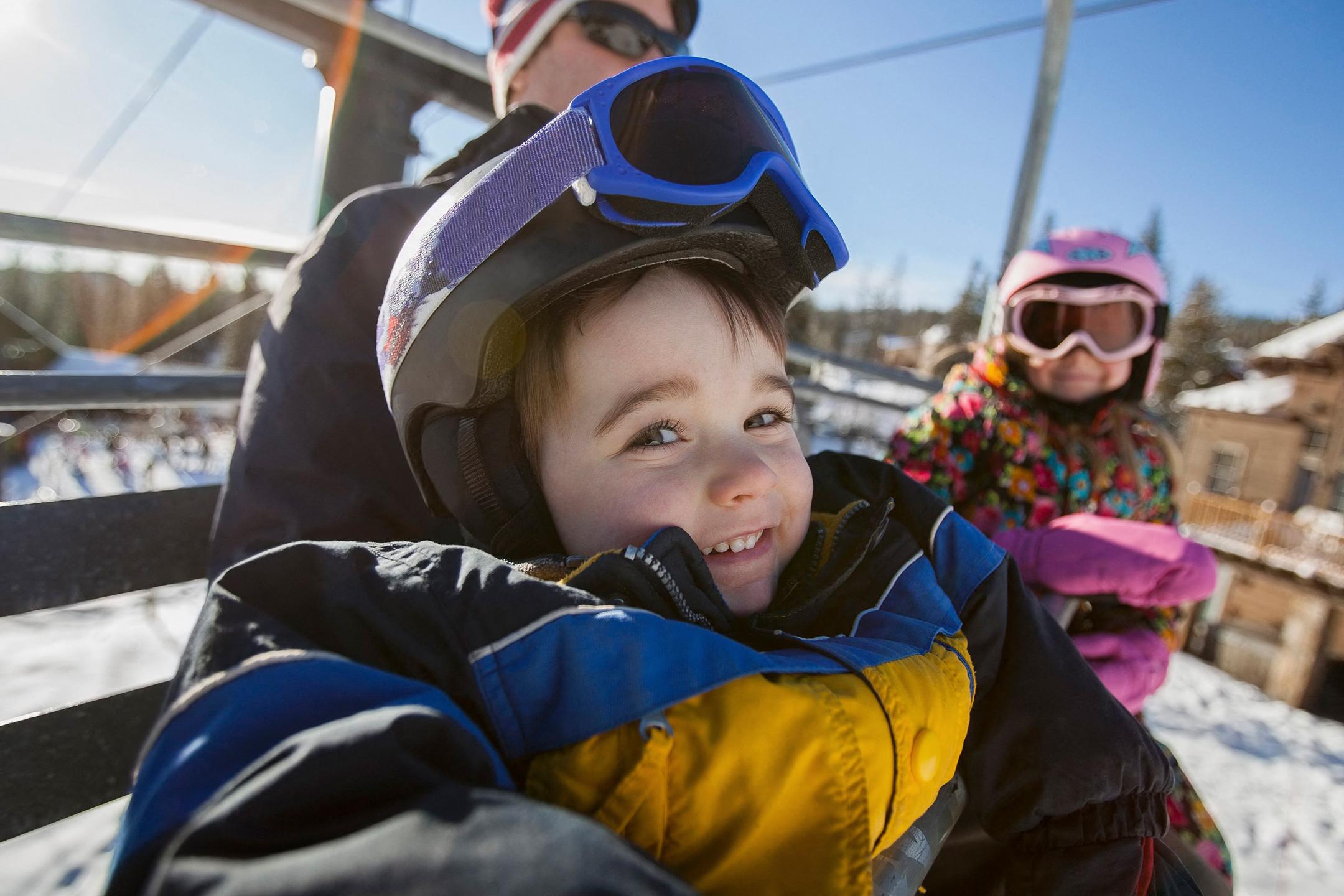 Un enfants est assis dans un télésiège emmitouflé dans sa combinaison de ski