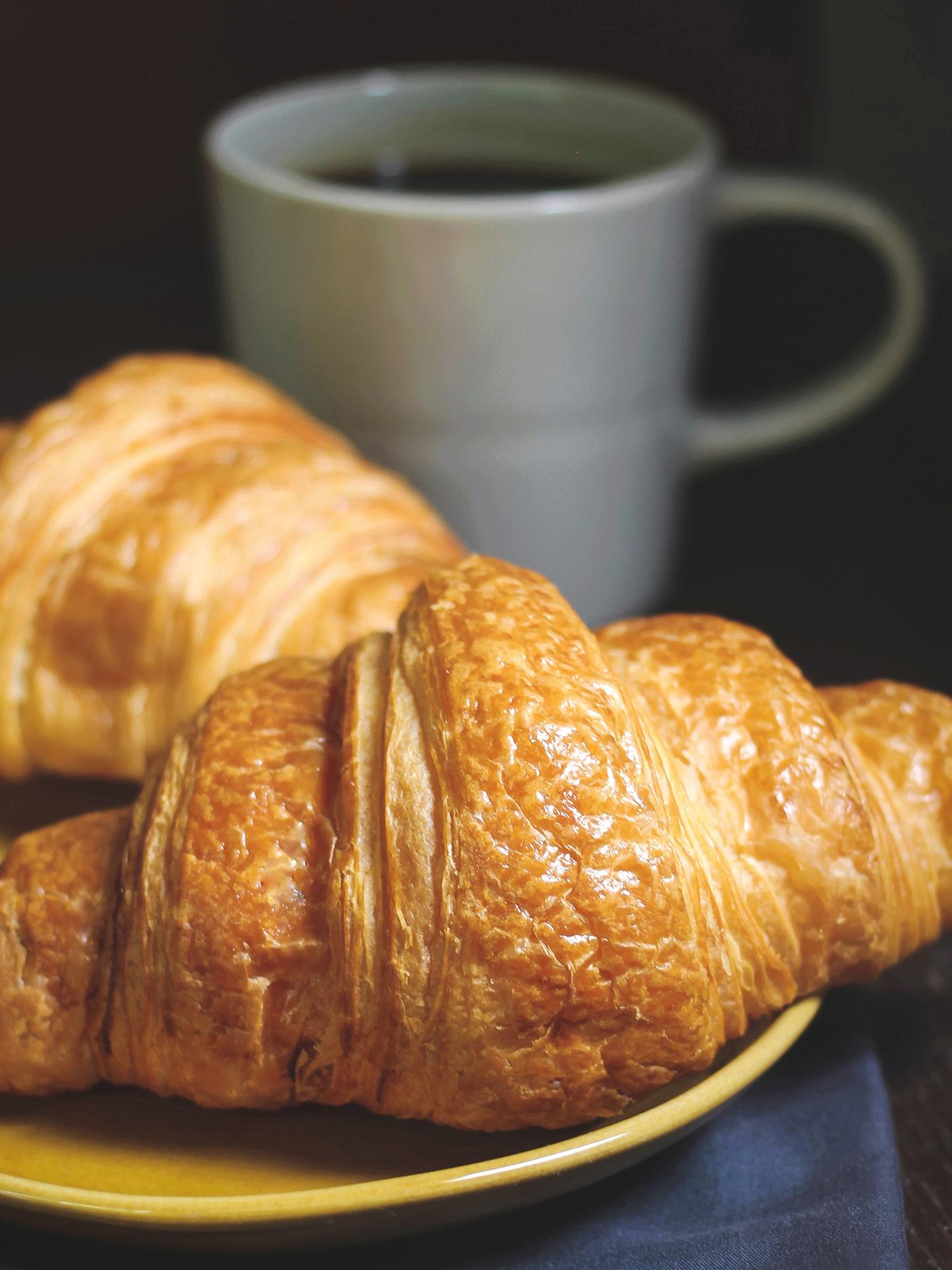 Un café est posé sur une table avec 2 croissants au premier plan 