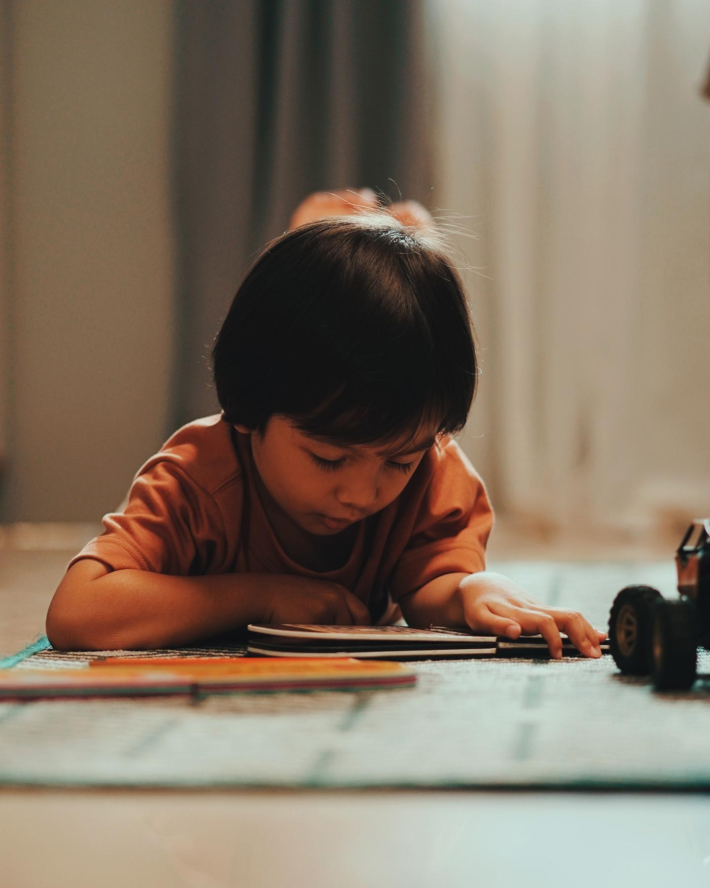 Un enfant est en train de lire un livre allongé par terre