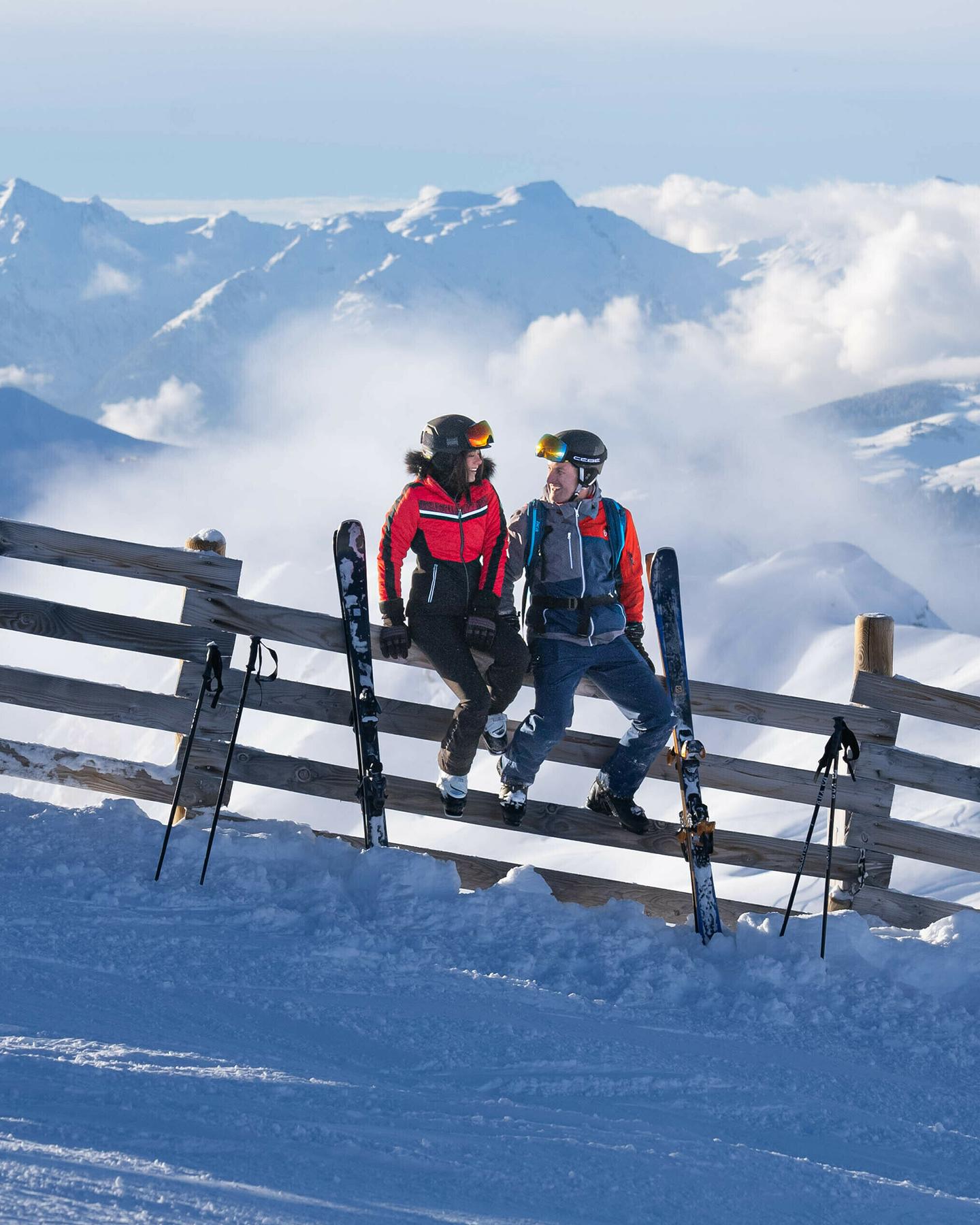 Un couple est assis sur une barrière en bois sur les pistes de La Plagne dans un décor enneigé