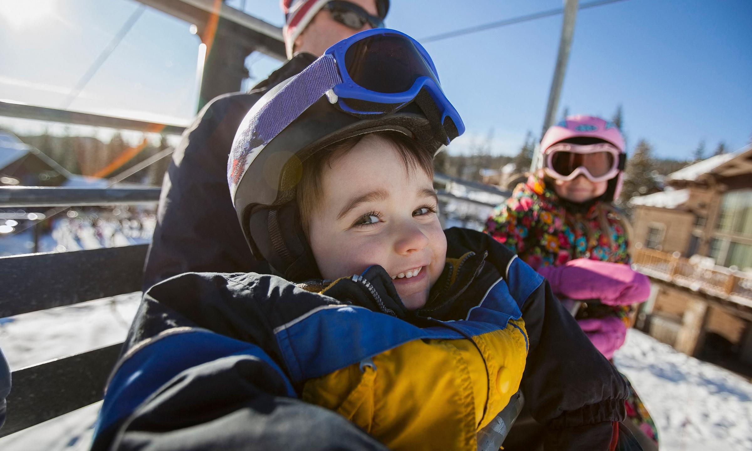 Un enfants est assis dans un télésiège emmitouflé dans sa combinaison de ski